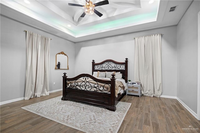 bedroom featuring ceiling fan, wood-type flooring, and a tray ceiling