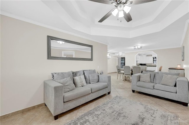 living area with a ceiling fan, a tray ceiling, light tile patterned flooring, arched walkways, and ornamental molding