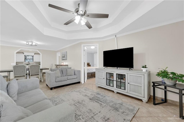 living area with ceiling fan, a tray ceiling, light tile patterned flooring, and ornamental molding