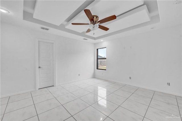 tiled empty room featuring ceiling fan and a tray ceiling