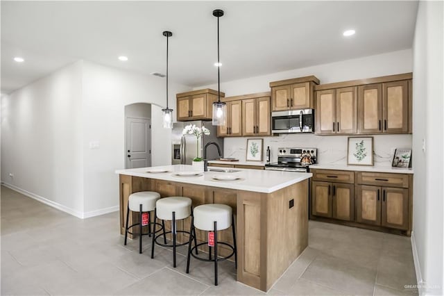 kitchen with appliances with stainless steel finishes, sink, a breakfast bar area, hanging light fixtures, and a center island with sink