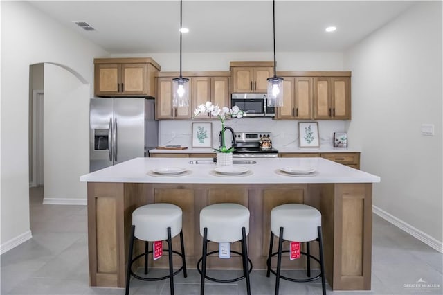 kitchen with a breakfast bar, sink, decorative light fixtures, appliances with stainless steel finishes, and an island with sink