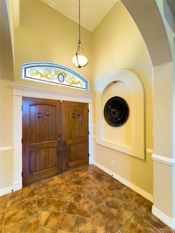 foyer entrance featuring arched walkways, baseboards, a high ceiling, ornamental molding, and stone finish floor