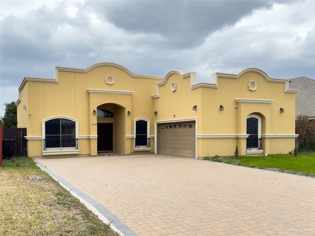 mediterranean / spanish-style home with a garage, decorative driveway, fence, and stucco siding