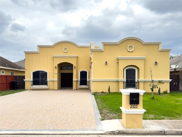 mediterranean / spanish home with a front lawn, decorative driveway, fence, and stucco siding