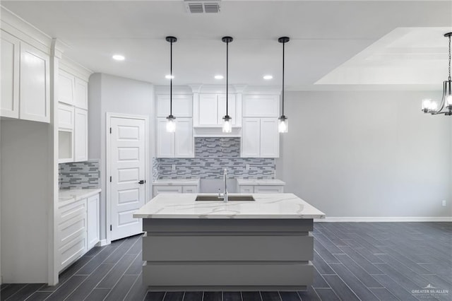 kitchen featuring light stone counters, white cabinetry, sink, and hanging light fixtures