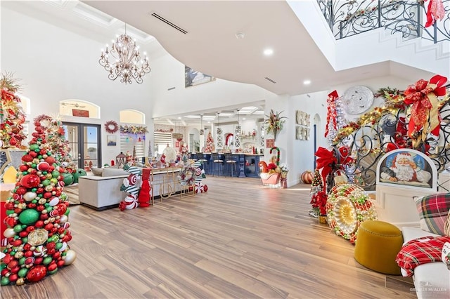 rec room featuring a towering ceiling, light hardwood / wood-style floors, and an inviting chandelier