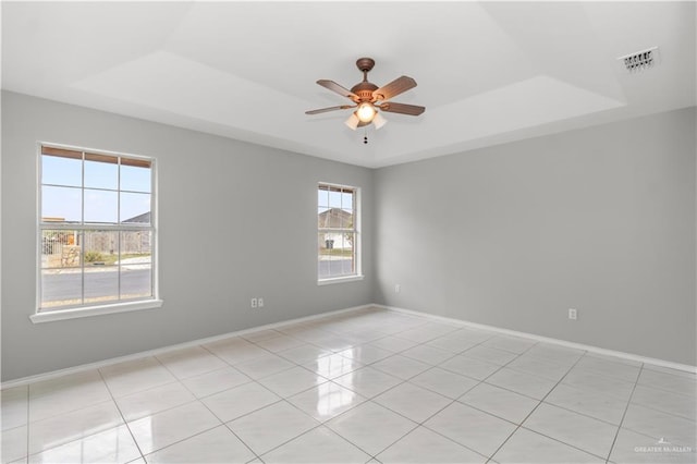 tiled spare room with ceiling fan and a tray ceiling