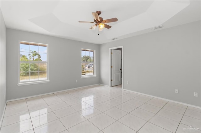 unfurnished room with a raised ceiling, ceiling fan, and light tile patterned floors