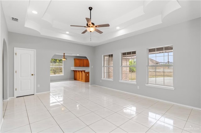 tiled empty room featuring ceiling fan and a raised ceiling