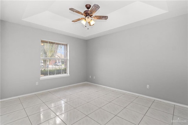 tiled empty room with ceiling fan and a raised ceiling