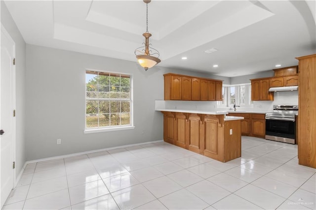 kitchen featuring a breakfast bar area, hanging light fixtures, stainless steel range oven, kitchen peninsula, and a tray ceiling