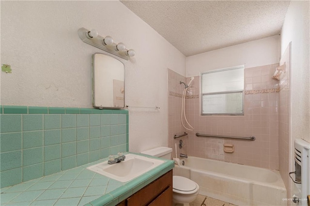 full bathroom featuring vanity, tiled shower / bath, toilet, a textured ceiling, and tile walls