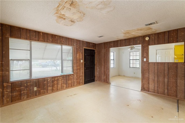 empty room with a textured ceiling, ceiling fan, and wooden walls