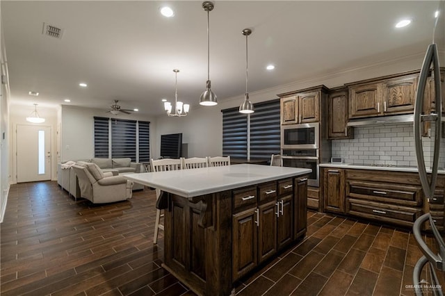 kitchen with decorative light fixtures, stainless steel appliances, tasteful backsplash, light countertops, and a kitchen island