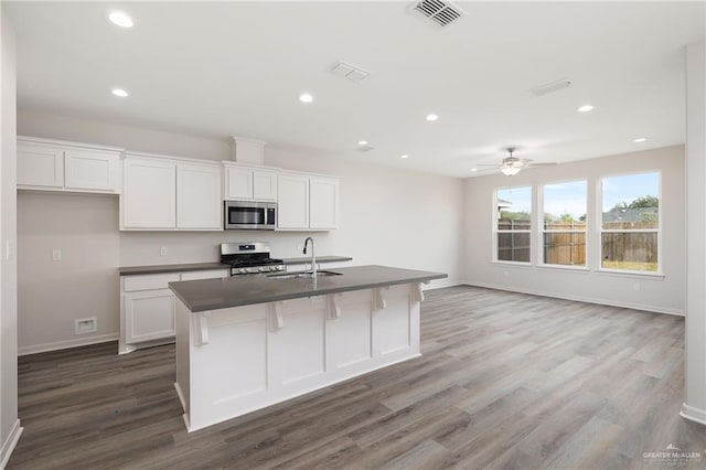 kitchen featuring visible vents, appliances with stainless steel finishes, dark countertops, wood finished floors, and a sink