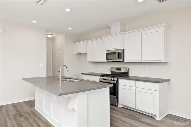 kitchen featuring light wood-style floors, a center island with sink, white cabinetry, a sink, and appliances with stainless steel finishes