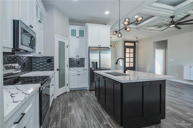 kitchen featuring glass insert cabinets, a sink, white cabinetry, appliances with stainless steel finishes, and a center island with sink