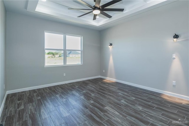 empty room featuring a ceiling fan, baseboards, a tray ceiling, and dark wood-type flooring