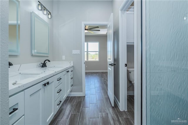 bathroom featuring toilet, a sink, baseboards, wood tiled floor, and double vanity