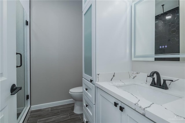 bathroom with toilet, a shower stall, vanity, and baseboards