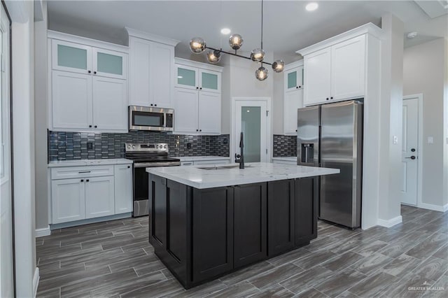 kitchen featuring an island with sink, glass insert cabinets, appliances with stainless steel finishes, white cabinetry, and a sink