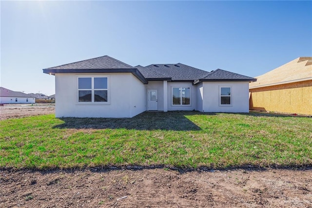 back of property with a shingled roof, a lawn, and stucco siding