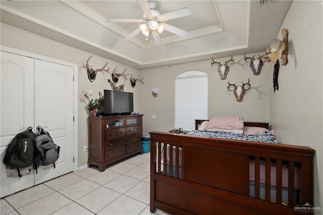 tiled bedroom featuring a tray ceiling, ceiling fan, and a closet