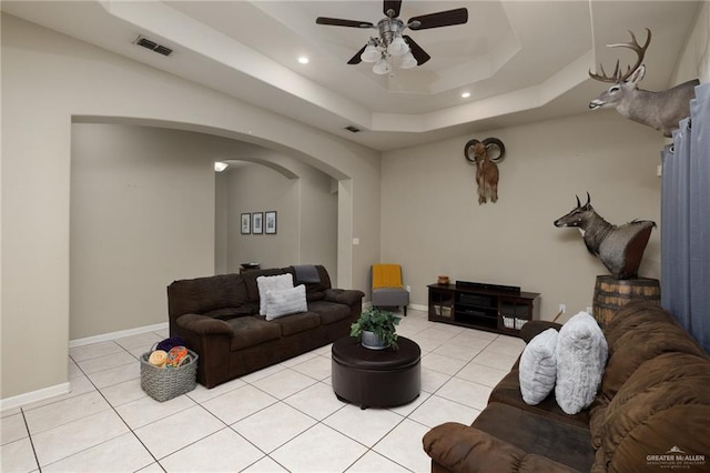 living room featuring ceiling fan, light tile patterned flooring, and a tray ceiling