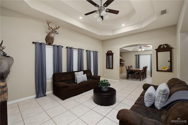 living room with ceiling fan, a raised ceiling, and light tile patterned floors