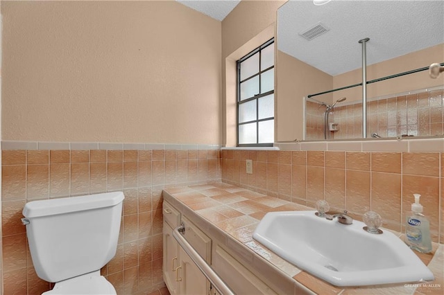 bathroom featuring a textured ceiling, vanity, tile walls, and toilet