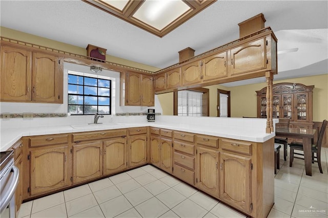 kitchen featuring kitchen peninsula, stainless steel range, sink, and light tile patterned floors