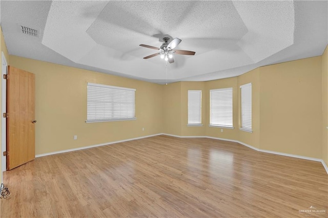 spare room with a textured ceiling, light wood-type flooring, ceiling fan, and a healthy amount of sunlight