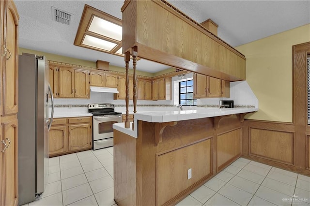 kitchen with kitchen peninsula, light tile patterned floors, a textured ceiling, and stainless steel appliances