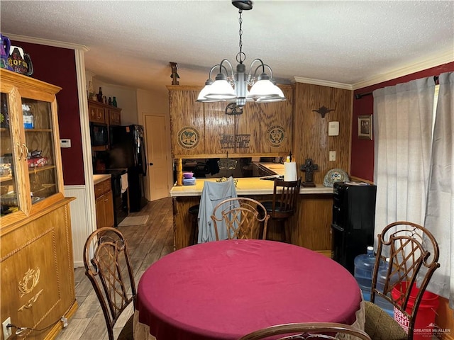 dining area featuring wood-type flooring, a textured ceiling, an inviting chandelier, and crown molding