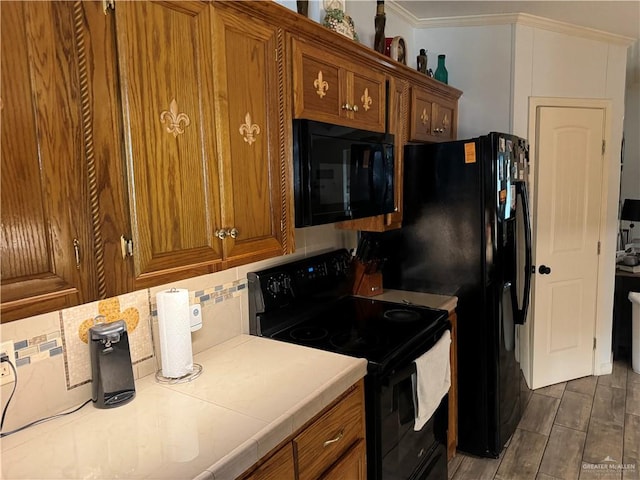 kitchen featuring decorative backsplash, crown molding, black appliances, tile countertops, and dark hardwood / wood-style floors