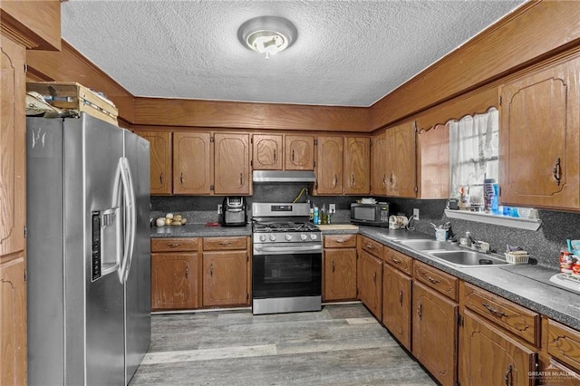 kitchen with backsplash, sink, light hardwood / wood-style flooring, a textured ceiling, and appliances with stainless steel finishes