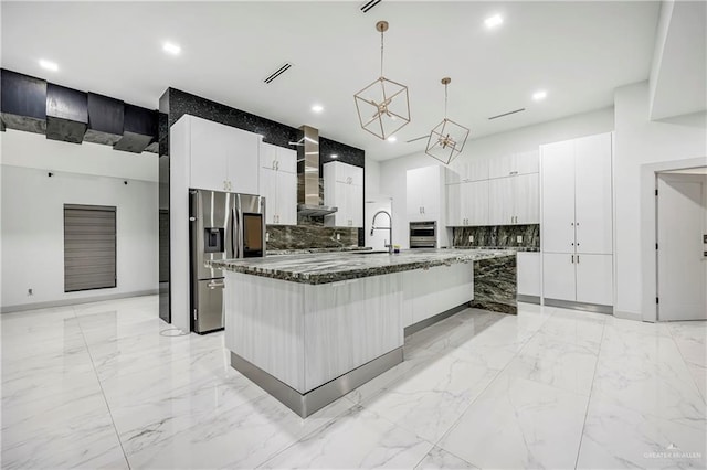 kitchen with a center island with sink, stainless steel appliances, wall chimney range hood, pendant lighting, and white cabinets