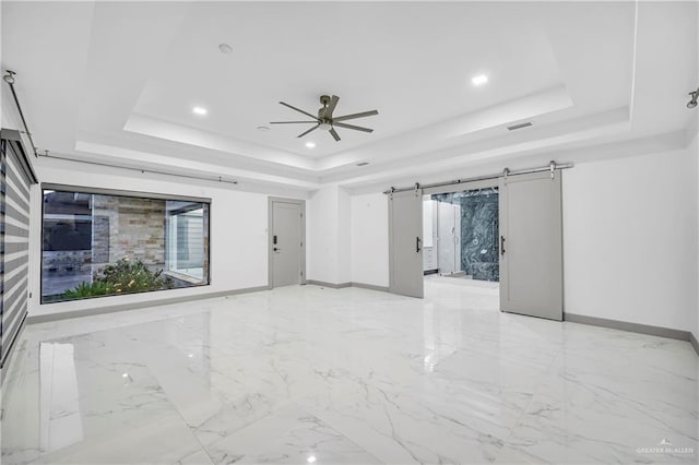 unfurnished room featuring ceiling fan, a raised ceiling, and a barn door