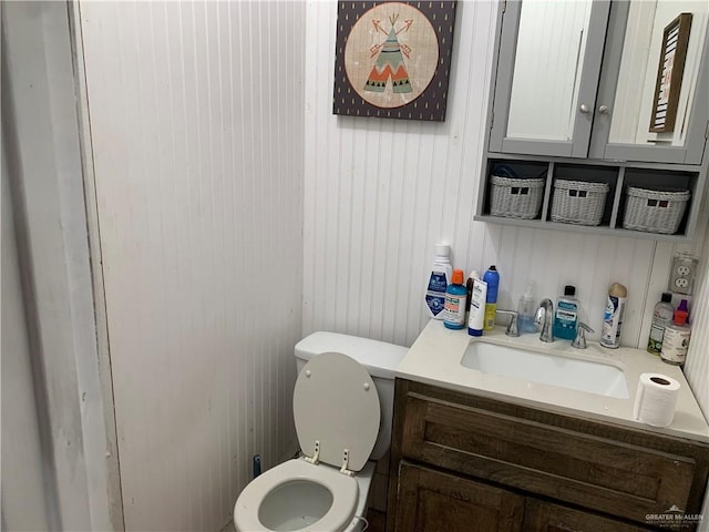 bathroom featuring wooden walls, vanity, and toilet