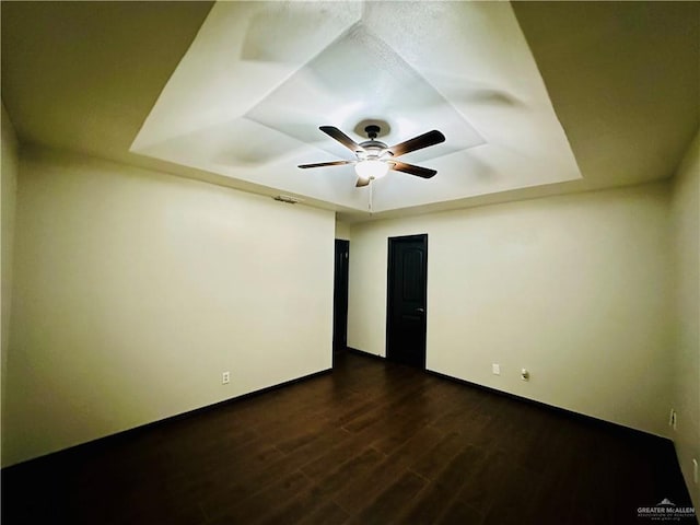 spare room with dark wood-type flooring, a raised ceiling, and ceiling fan