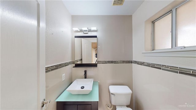 bathroom with vanity, toilet, and tile walls