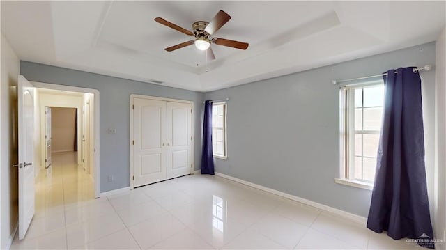 unfurnished bedroom featuring light tile patterned flooring, ceiling fan, a raised ceiling, and a closet