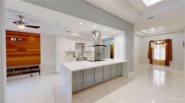 kitchen with sink, white cabinetry, an island with sink, island exhaust hood, and a raised ceiling