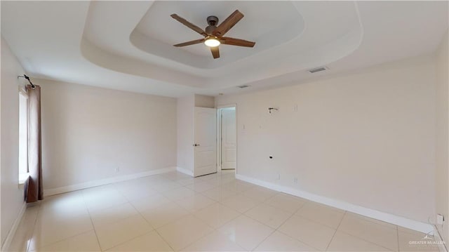 empty room with light tile patterned floors, ceiling fan, and a tray ceiling