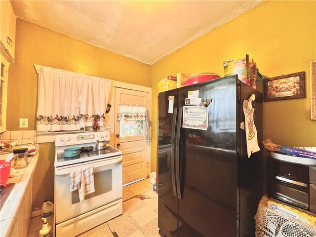 kitchen with electric range, tile counters, and black refrigerator with ice dispenser