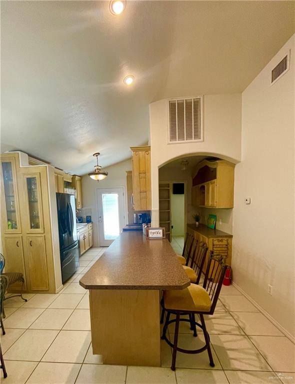 kitchen with black refrigerator, a kitchen breakfast bar, kitchen peninsula, and vaulted ceiling