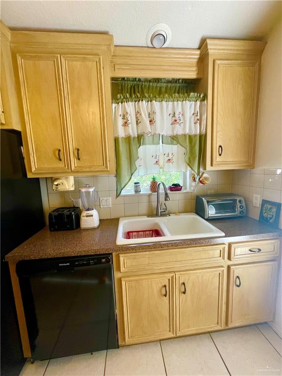 kitchen with backsplash, sink, light tile patterned floors, and black appliances