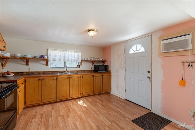 kitchen with light wood finished floors, a wall unit AC, black appliances, open shelves, and a sink