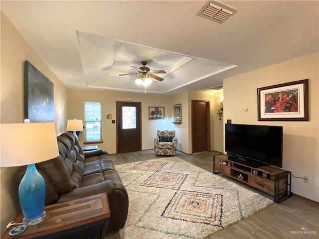 living room with ceiling fan, wood-type flooring, and a tray ceiling